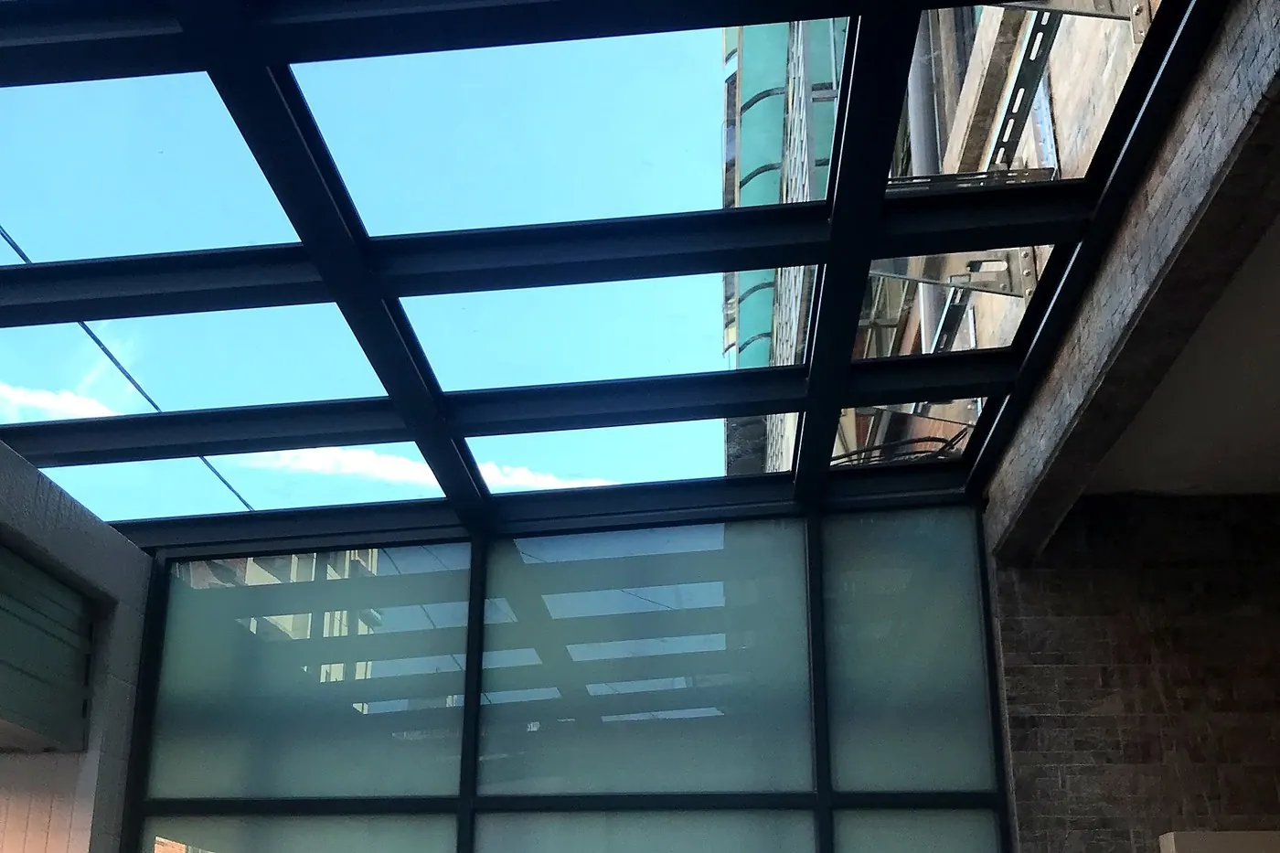 側院上方是深色骨架的玻璃頂，側面是霧面玻璃牆，圍成半室內的空間